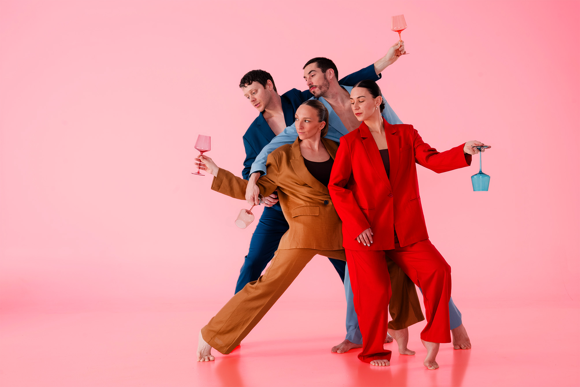 Les quatre interprètes lèvent leurs verres sur un fond rose, en costumes bleu, rouge et ocre